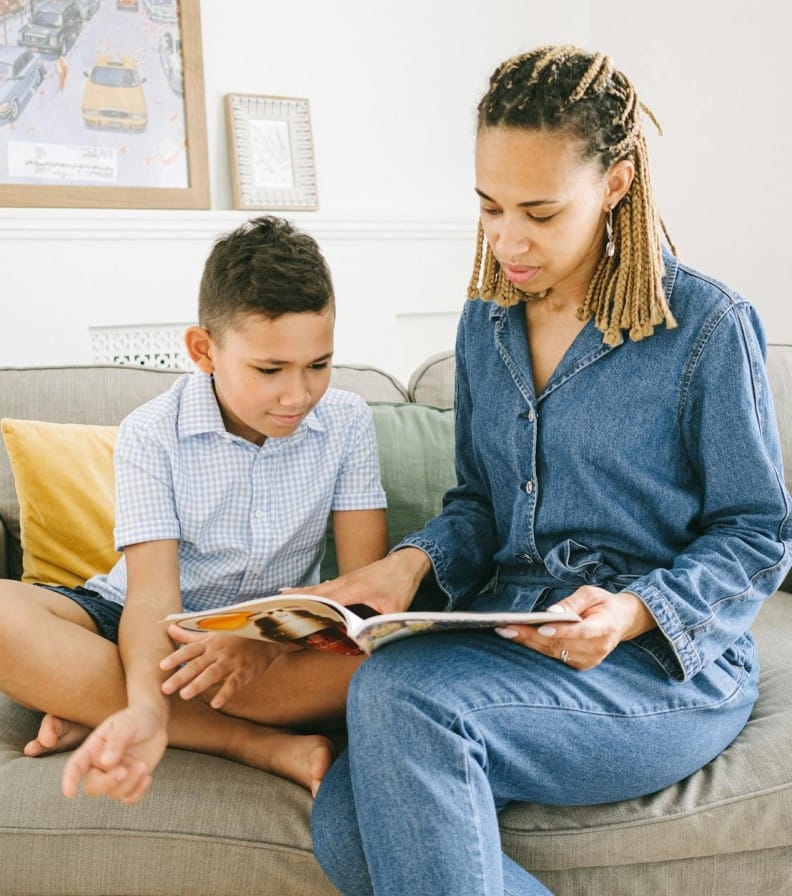 A mother and her son share quality time reading a book together on the couch in a cozy room.