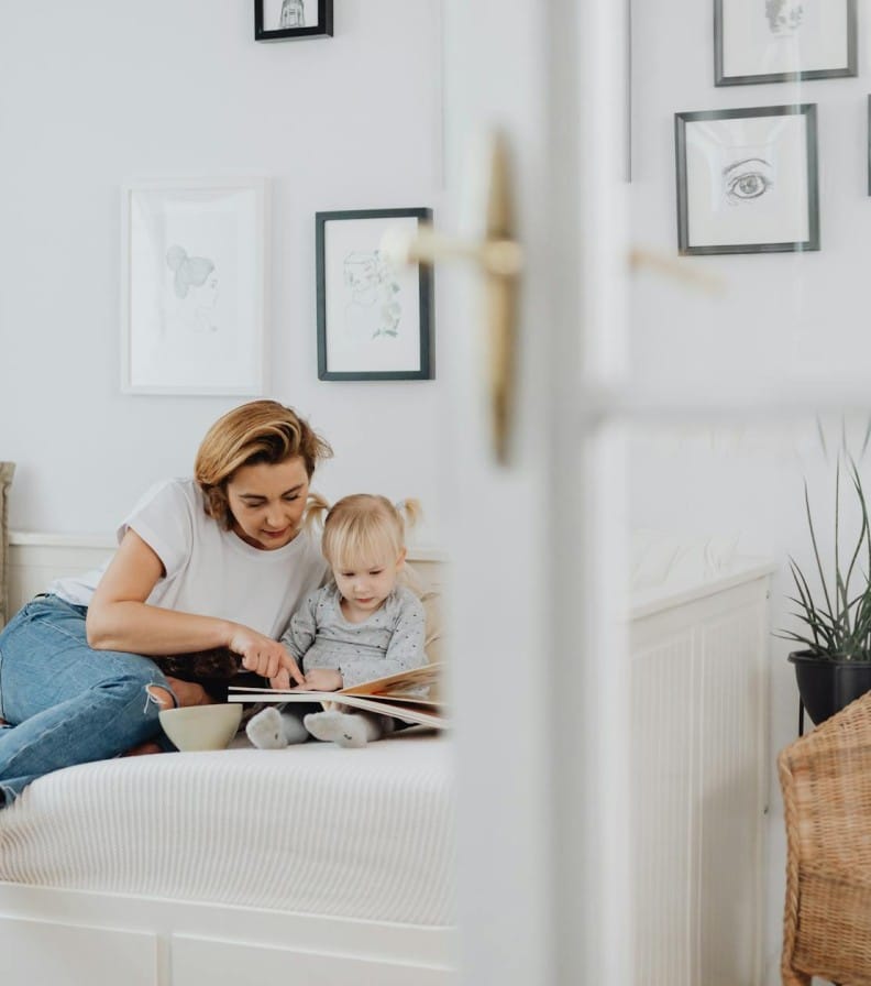 A mother and daughter enjoy reading a book together in a cozy living room setting.