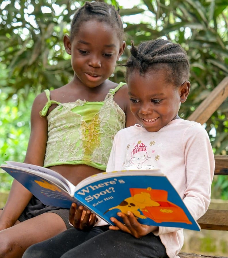 Two children enjoying a storybook outdoors, sharing a joyful reading moment.