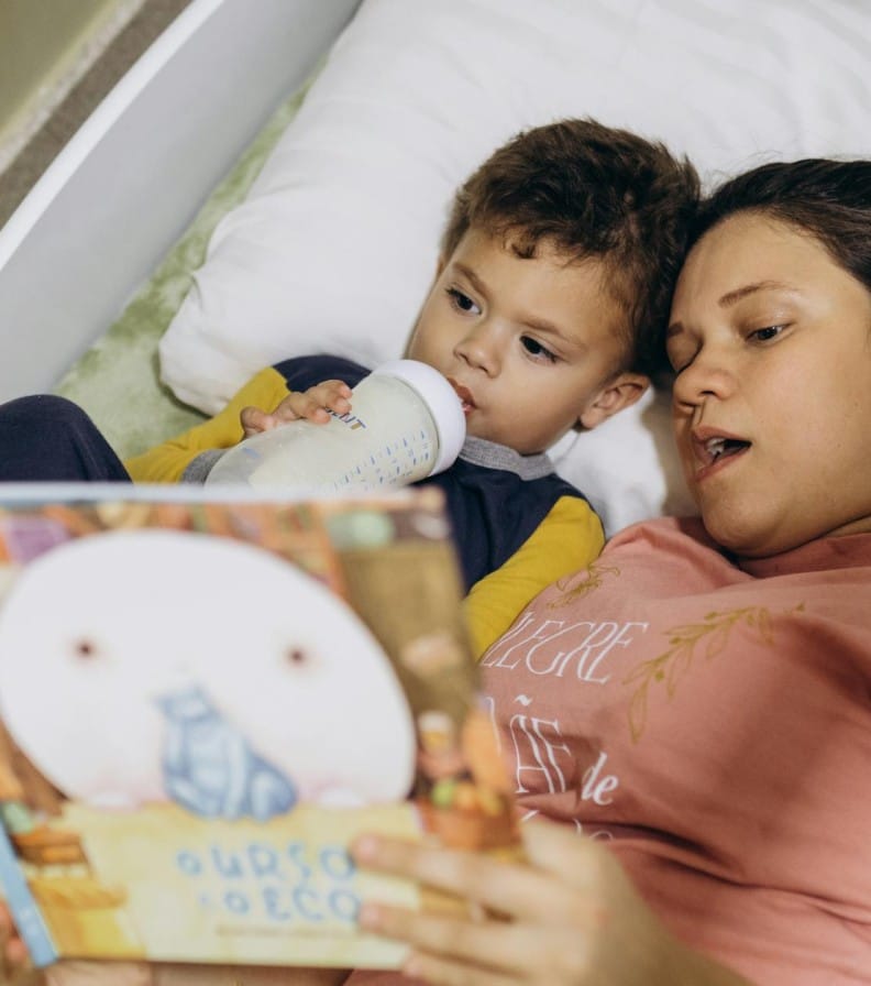 A mother reads a bedtime story to her child while he drinks milk, creating a cozy and bonding moment.