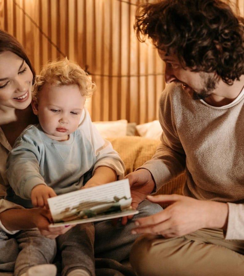 A joyful family bonding moment with parents and child reading in a cozy indoor setting.