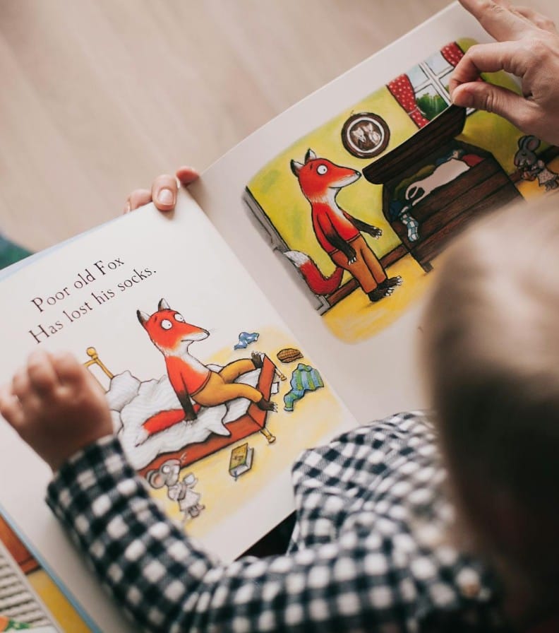 A child and adult reading an illustrated storybook together in a cozy setting.
