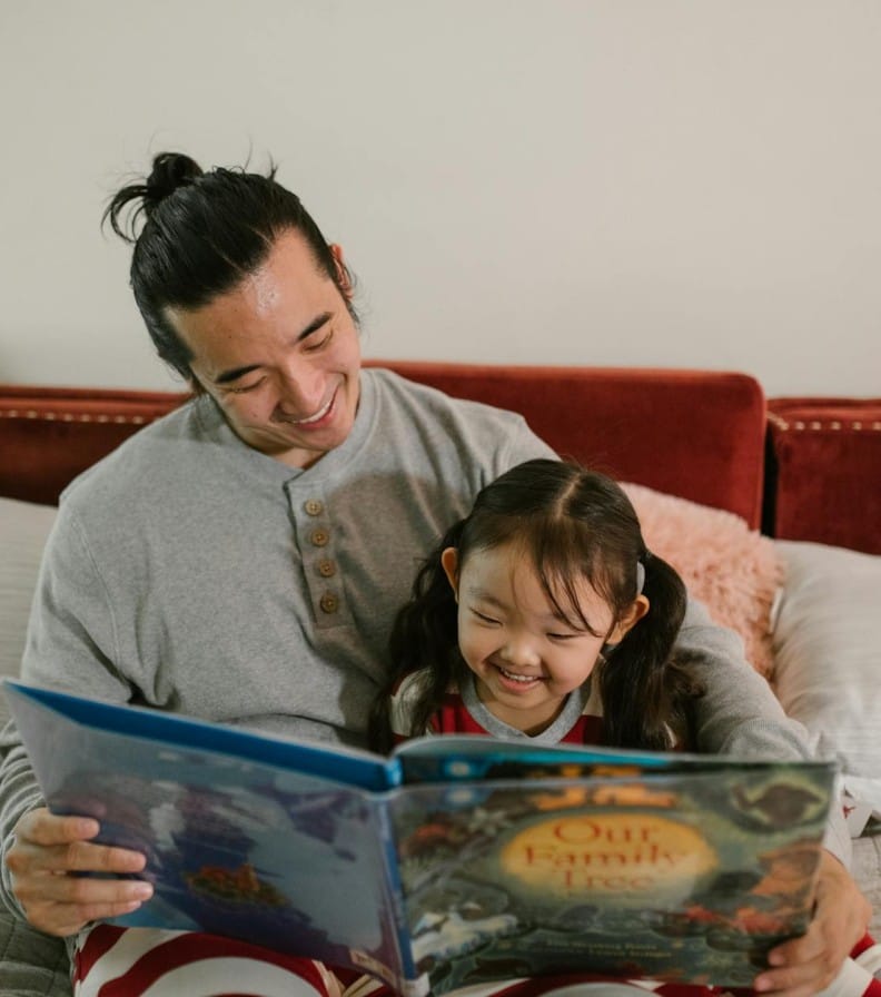 A joyful father and daughter reading a storybook in a cozy bedroom setting, sharing a happy moment.
