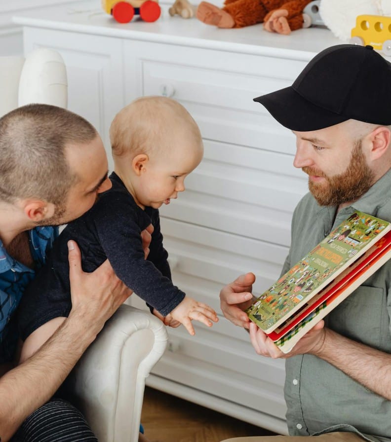 A loving same-sex couple engages in a storybook session with their baby indoors.