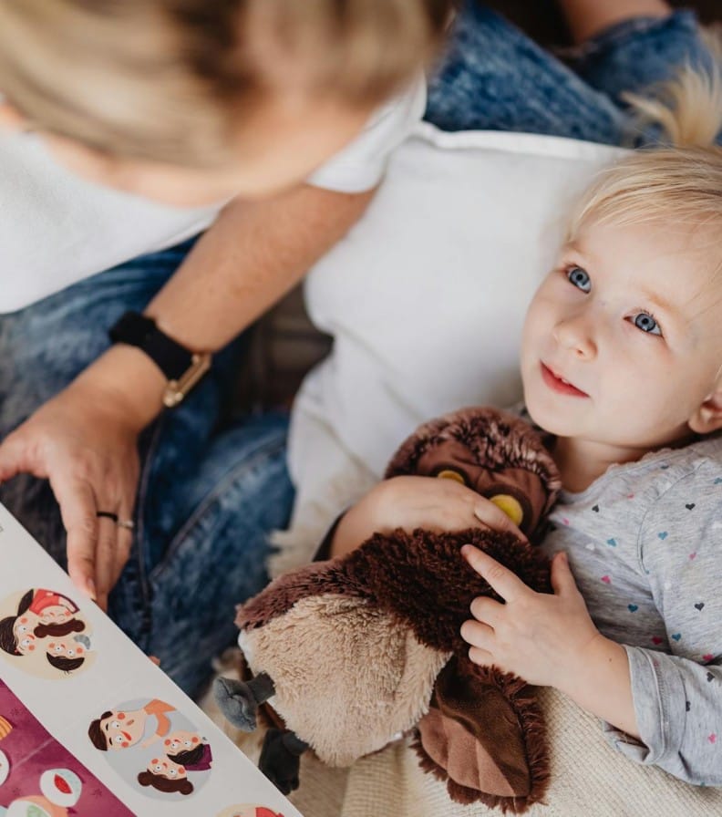 A mother reading a storybook to her toddler daughter indoors, depicting a cozy storytelling moment.
