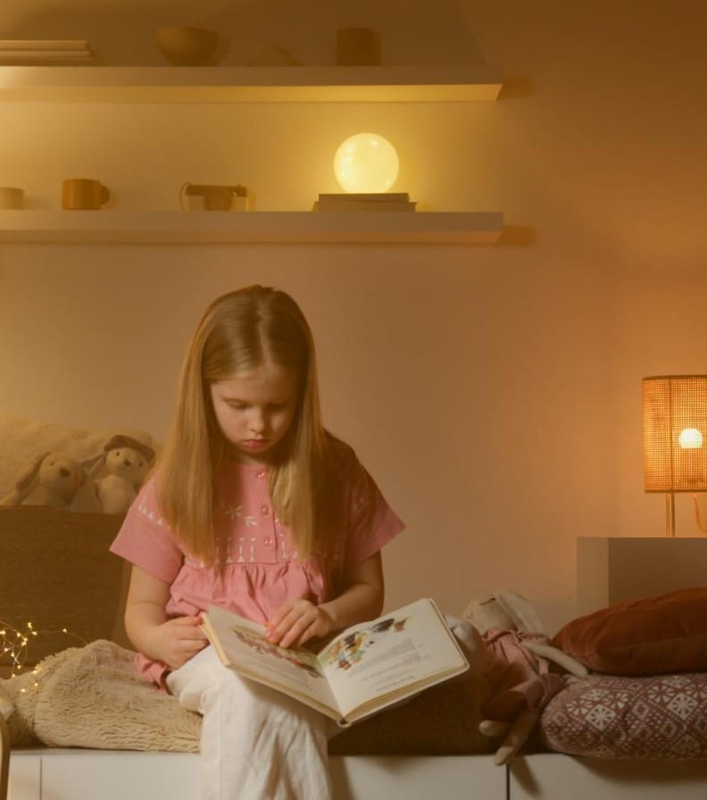 A young girl reading a book in a warmly lit bedroom, creating a cozy and calm atmosphere.